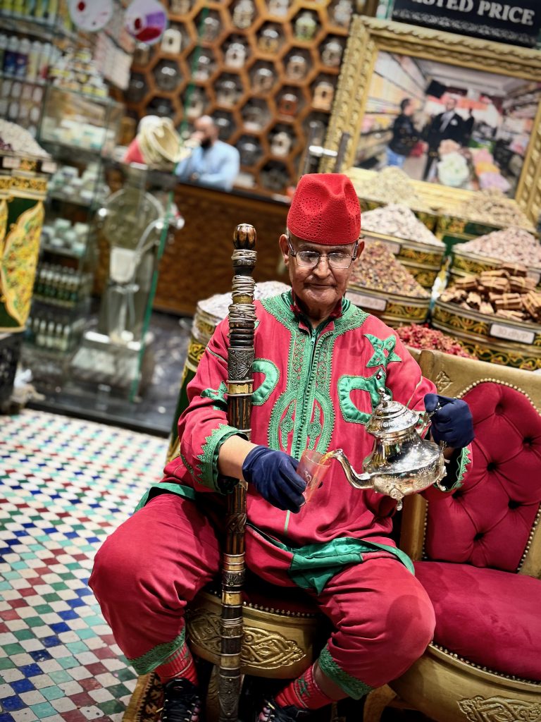 An elderly man in traditional Moroccan attire gracefully pouring tea from a silver teapot, showcasing the artistry and cultural significance of Moroccan tea rituals.