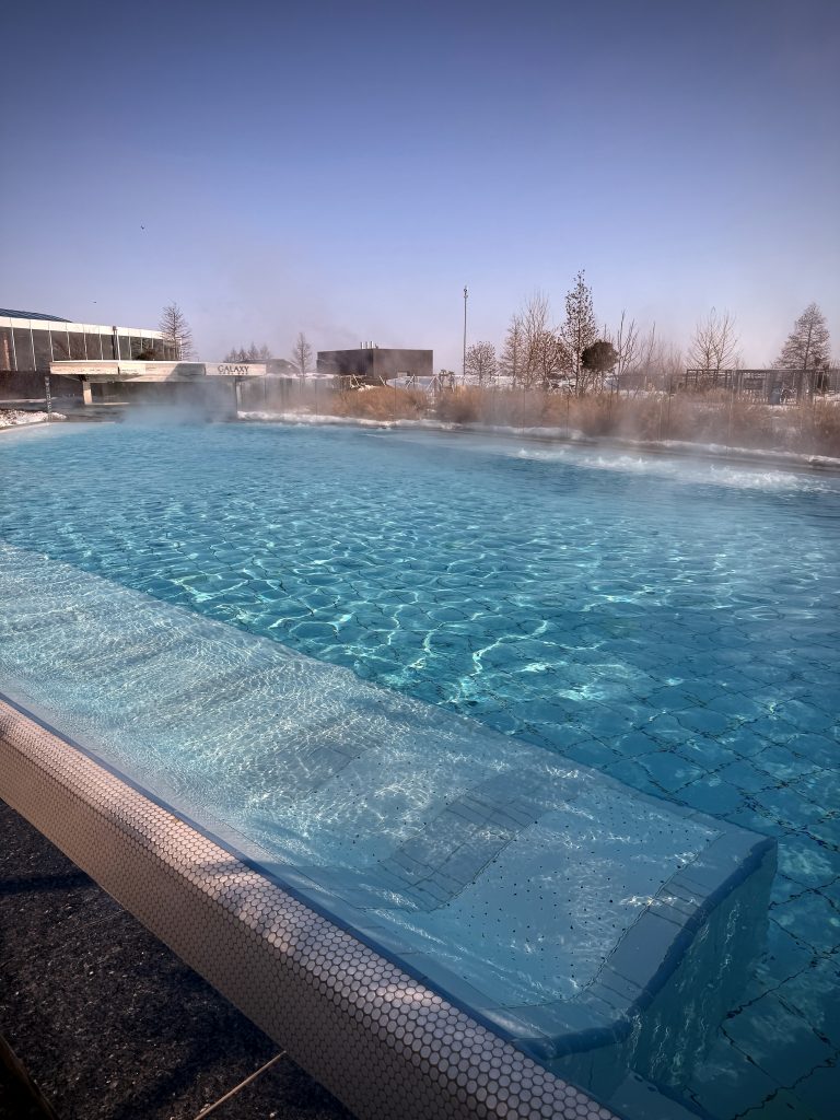 A steaming outdoor thermal pool at Therme Bucharest, surrounded by snow with clear blue skies overhead.