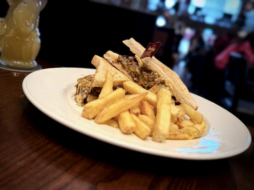 Close-up of the Patty Melt dish at Hard Rock Cafe Manchester, featuring two burger patties between under-toasted white sandwich bread, served with a large portion of thick-cut fries on a plain white plate.