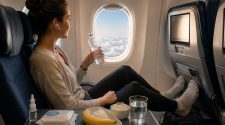 Woman sitting in an aeroplane window seat with water, banana, rice and nasal spray while following long-haul flight health tips.