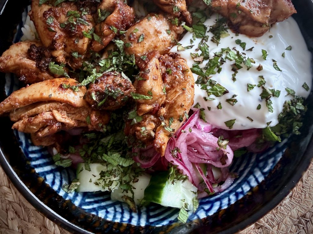 Close-up of a chicken shawarma rice bowl with spiced chicken thighs, garlic yoghurt, pickled red onion, cucumber and fresh herbs.